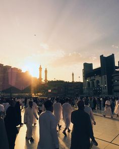 a group of people walking down a street in the middle of a city at sunset