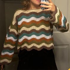 a woman taking a selfie in front of a door wearing a colorful knitted sweater