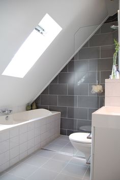 a white toilet sitting in a bathroom next to a bath tub under a slanted ceiling