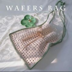 a crocheted bag sitting on top of a white bed next to a green flower