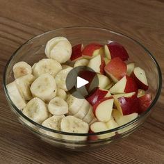 a glass bowl filled with sliced up bananas and apples on top of a wooden table