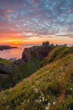 the sun is setting over an island with cliffs and flowers on it's side