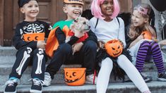 three children in halloween costumes sitting on the steps with their dog and pumpkin buckets