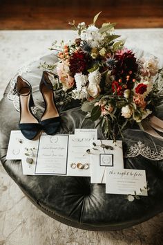 a bouquet of flowers and wedding rings on a black leather ottoman with matching shoes for the bride