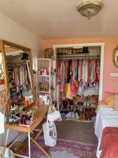 a bedroom with pink walls and lots of clothes hanging on the closet doors, along with a large mirror