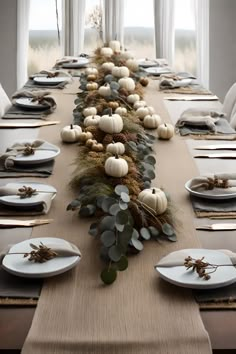 a long table with white pumpkins and greenery on it, along with place settings