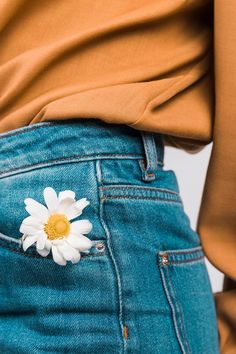 a woman's jeans with a daisy in the pocket and a brown shirt behind her