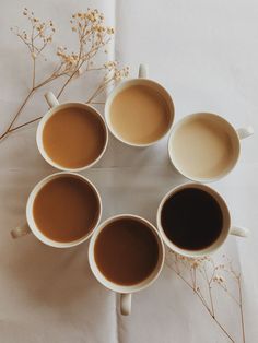 six cups of coffee are arranged in the shape of a circle on a white tablecloth