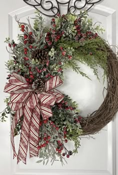 a wreath hanging on the front door with red berries and evergreens tied to it