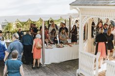 a group of people standing around a table with food on top of it and in front of a white gazebo