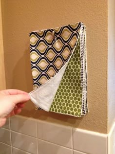 a person is holding three pieces of fabric in front of a tiled wall