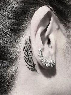 a woman's ear has a small feather tattoo on it