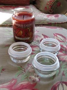 three glass jars sitting on top of a floral table cloth next to a lit candle