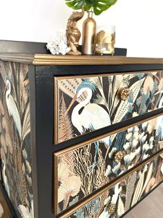 an ornate painted dresser with flowers and birds on the drawers, next to a potted plant