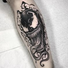 a black and white tattoo with an alien head on the arm, holding a snake in its mouth