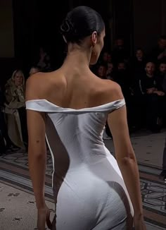 a woman in a white dress is walking down the runway with her back to the camera