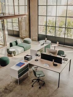 an office area with couches, desks and chairs in front of large windows