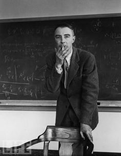 a man standing in front of a blackboard with writing on it and holding his hand to his mouth