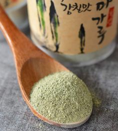 a wooden spoon filled with green powder next to a jar