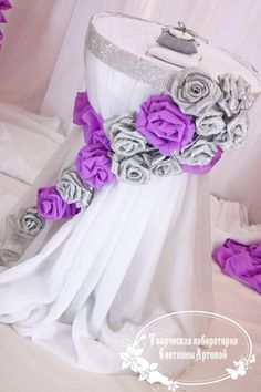 a white dress with purple flowers on the waist and bottom, is sitting on a bed