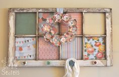 an old window frame is decorated with paper and magnets as a wreath hangs on the wall