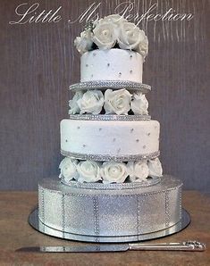 a three tiered wedding cake with white roses on top and silver ribbon around the edges