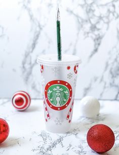 a starbucks cup with a green straw in it next to christmas ornaments and baubies