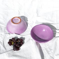 two purple bowls and grapes on a white sheet