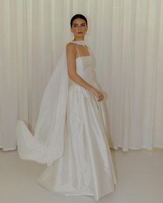 a woman in a white wedding dress standing next to a curtain with her veil pulled back