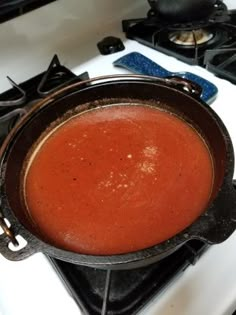 there is a pot on the stove with red liquid in it and some other items nearby