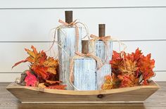 a wooden boat filled with fall leaves and twine wrapped candles on top of it