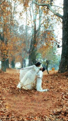 a bride and groom are kissing in the woods with leaves on the ground around them