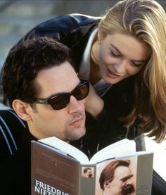 a man reading a book with a woman leaning over him to look at the book