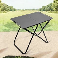 a black folding table sitting on top of a blanket in the middle of a field