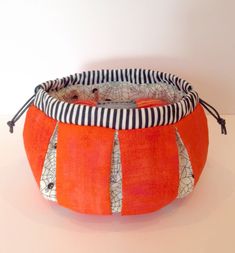 an orange and black striped basket with spider webs on it, sitting on a white surface