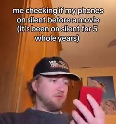 a man holding a red cell phone in his right hand and looking at it with the caption'me checking if my phones on silent before a movie it's been on silent for 5 whole years