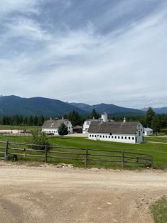 a large white barn sitting next to a lush green field with mountains in the background