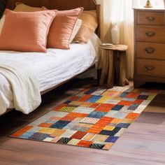 a bed sitting next to a wooden dresser on top of a hard wood floor covered in pillows