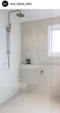 a white tiled bathroom with a shower head and glass door, along with a window