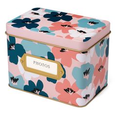 a pink and blue flowered box sitting on top of a white surface with a gold label