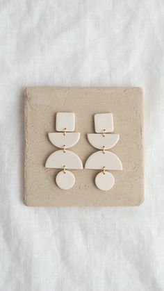 two white and gold earrings sitting on top of a piece of paper