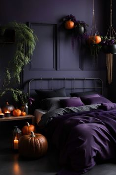 a bed with purple sheets and pumpkins on the floor in front of a black wall