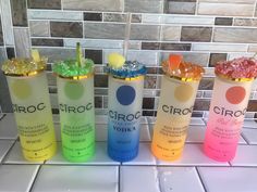 four different flavored drinks are lined up on the tiled countertop in front of a mosaic tile wall