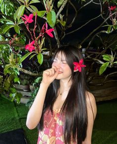 a woman standing in front of a tree with pink flowers on her hair and eyes closed