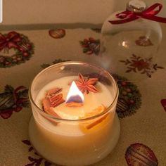 a lit candle sitting on top of a table next to a glass jar filled with cinnamons