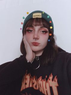 a girl with piercings on her nose wearing a black shirt and a green hat