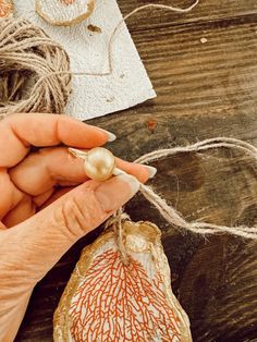 a woman is working on something with some string and beads in her hand while sitting at a table