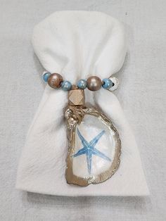 a white bag with a blue starfish charm on it's side and a beaded necklace hanging from the front