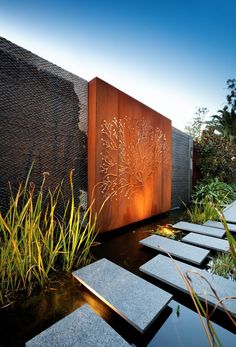 an outdoor area with benches, plants and water features in the background is a large metal screen