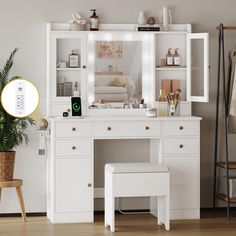 a white dressing table with mirror and stool next to potted plant on wooden floor